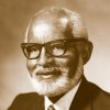 Older African-American man with glasses and beard smiling in suit and tie