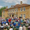 Crowd of people with folding chairs gathered around a multistory stone building in town square