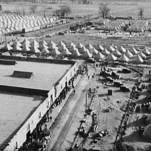 Aerial view people line up by building near trucks and rows of more than 100 tents