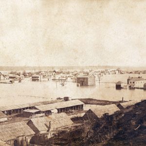 Flooded town viewed from hill top by wood frame barns and ridge in distance