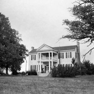 Two-story wood frame home with porch balcony chimneys large front yard shrubs and trees