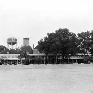 Building complex cars trees street field foreground old and new water towers background painted "VA"