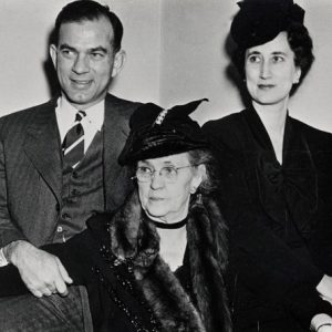 One white man two women in formal wear sit closely together man's hand on woman's arm