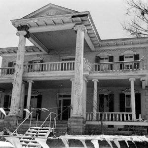 Two story home with large chipped paint columns porch balcony temporary metal stairs pennant banners