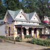 Stone building with sign "Gann Museum," wooden gables, covered porch, garden along street.