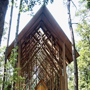 Narrow wood frame building with A-frame roof and hanging glass walls in wooded area