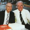 White men seated in suit ties pose smiling by bus with table book display