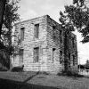 Austere two story stone building with window bars lawn trees nearby shed barn