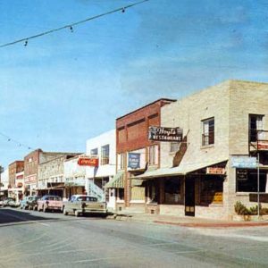 Street with brick buildings, parked cars, overhanging string lights and various business signs