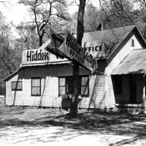 Wood frame house in woods with signs reading "Hidden Valley Office"