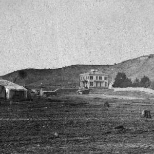 Dirt field with tree stumps and barns multistory home fence and ridgetop and building far in background