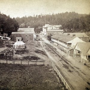 City road in valley with wood frame buildings hotel tent man walking and mountain background