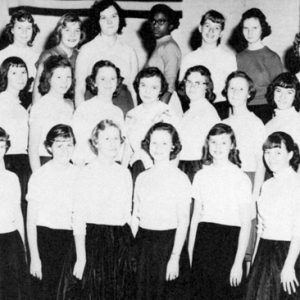 Group school photo with matching white girls and one black girl on bleachers below flag