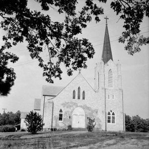 tall brick church with high steeple with a cross on top gothic arched windows arched doorway