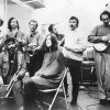 five people with instruments and two without standing and sitting in studio