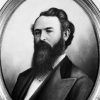 oval-framed portrait of a white man with dark hair and a long beard wearing a suit