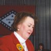 white woman in red coat in front of Arkansas state flag