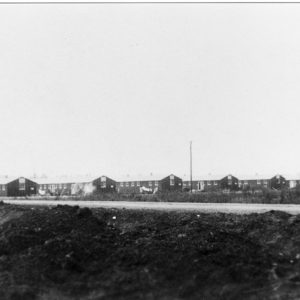 Row of long windowed barracks with power lines by road