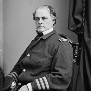 White man sitting in military uniform with cap and curtains behind him