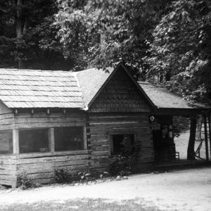 Single-story cabin with screened windows and covered porch under a tree