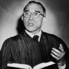 Portrait white male judge in robe speaking holding book hand raised spot lit