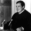 white man in black robe speaks into several microphones at lectern