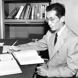 Japanese-American man in suit and tie reading at his desk