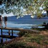 Two white people standing on a wooden boat dock on large lake surrounded by mountains