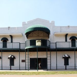 Two-story building with green balcony and awnings above covered walkway with street lamps