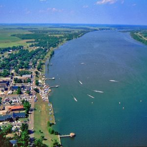 Town buildings on multilane streets next to large lake with countryside in the background as seen from above