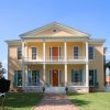 Two-story house with covered porches balconies and framed windows on grass with brick walkway