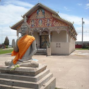 Single-story brick temple building with statue of Buddha on pedestal in the foreground