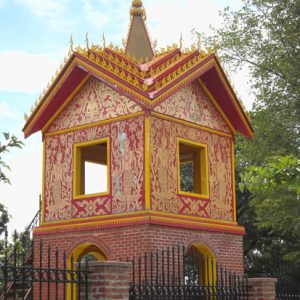 Brick tower with red and yellow detailed walls inside iron fence with brick columns