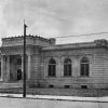 wide stone building with arched windows on each win, columns flanking entrance, situated on street corner