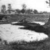 Water filled pit with multistory house in the background