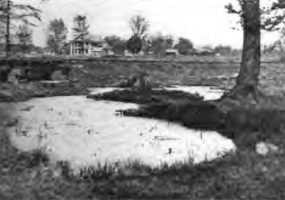 Water filled pit with multistory house in the background