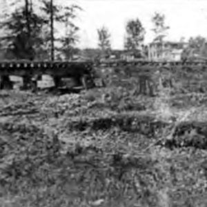 Bridge over drained pit with trees and multistory house in the background