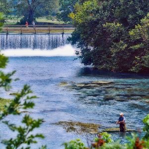 man fly fishing with waterfall and pedestrians in background