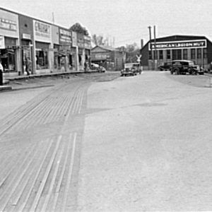 Street with stores on the left looking towards the "American Ligion Hut" building