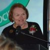 White woman with corsage speaking at a lectern