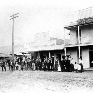 Group of people with one on horseback posing outside hotel