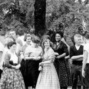 African American teen stands amongst crowd of white teens with soldiers behind