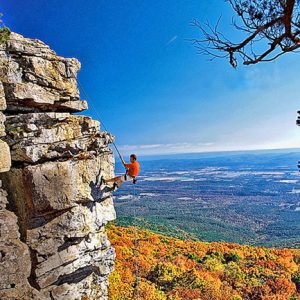 man climbing striated rock face overlooking fall trees