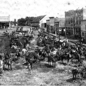 Numerous horses with riders in street with buildings in background