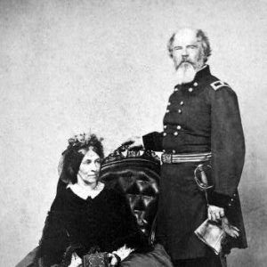 Portrait photo of a seated woman in a formal dress holding a book with a bearded man in a military uniform and sword standing with his hand on her chair