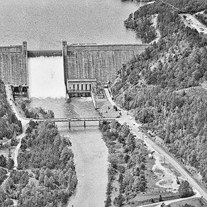 Concrete dam on river with tree covered hills and bridge in the foreground