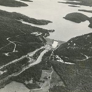 Lake and concrete dam in tree covered countryside as seen from above