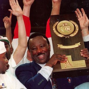 smiling African American man holds up wooden and golden trophy among other celebrating men