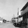 Storefronts and cars on town street with power lines