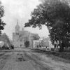 tree-lined wide dirt road leading to multistory building with steeples and clock tower